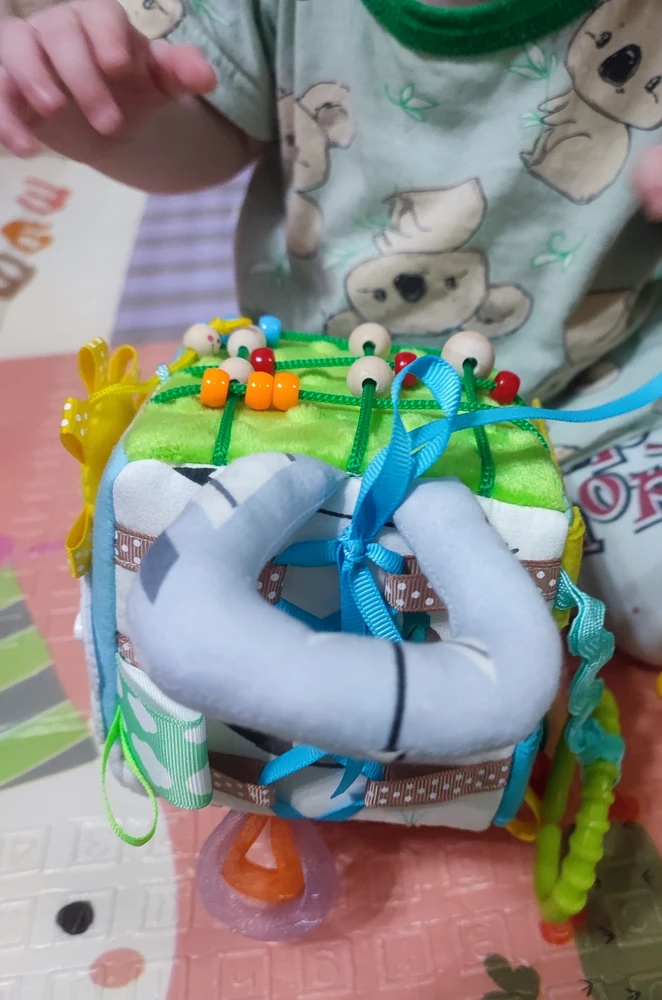 Мадемуазель 8 месяцев, заинтересовалась бизиком только на 2-ой день, нравится солнышко и бусинки.

Сам бизиборд классный, продуман до мелочей, застёжки, ленточки, пуговички, липучки, ручки для удобства - короче всё основное, с чем столкнется малыш в будущем. Мягкий, но в то же время упругий, можно будет в будущем брать с собой в поездки, например. Бусины и кольцо идеально зашлифованы.
Перед тем, как дать ребенку куб, сначала подергала его сама, особого доверия не вызвала голубая пуговичка только, но и это не проблема, потому что такую вещь без присмотра все равно не дам поиграть/погрызть.
Покупка обошлась в 1750р: фурнитура, ручная работа (не придраться, во всяком случае к нашему кубику), затраченное время на создание - денег не жаль. Ну и купила бы я его ещё раз? Определенно. 
Спасибо вам, автор, за ваш труд. Классная вещь ❤️